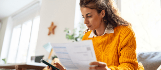 Woman sitting on couch at home looking at bills and phone