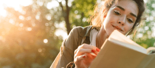 Woman reading a book outside surrounded by trees