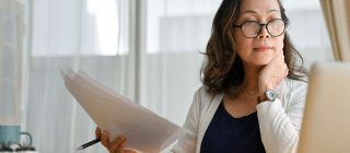 Woman holding papers, looking at laptop