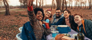 group of friends sharing a meal outside, taking a selfie