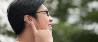 man standing outside pointing to his hearing aid