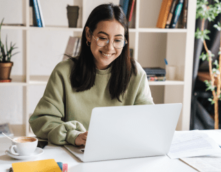 young woman looking at laptop with book shelf behind her